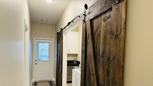A hallway with a wooden barn-style door leading to a kitchen area. - Luxury Medical District Home, EV Charger, Gated #10 (Augusta)