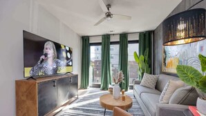 Een moderne woonkamer met een flatscreen televisie, een plafondventilator, een bank, een salontafel en een groot raam met gordijnen.