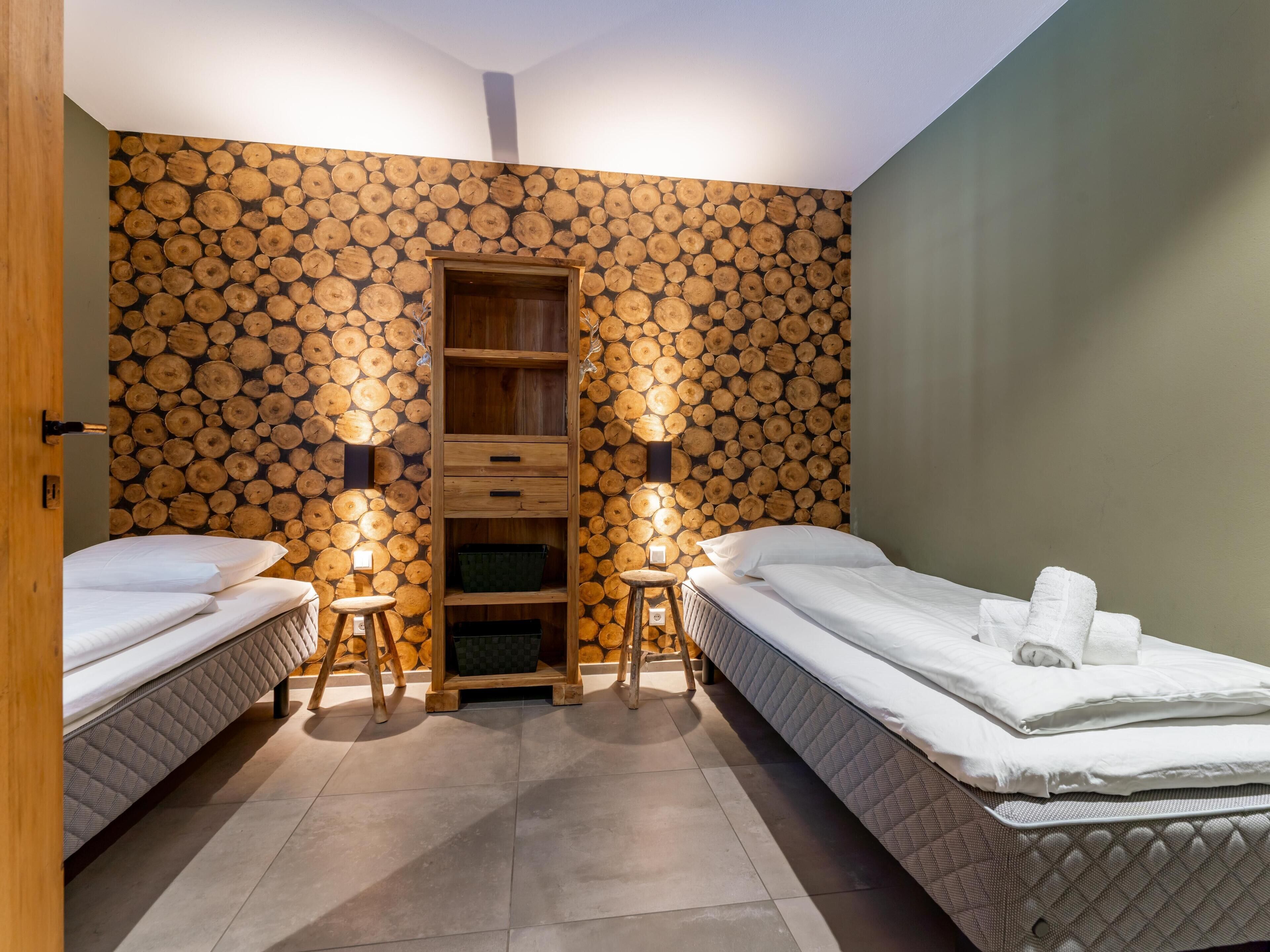Een kamer met twee bedden, een houten trap en een muur bekleed met boomstammen.