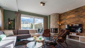 A modern living room with a stone fireplace, leather chairs, a sofa, and a flat-screen TV.