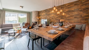 A modern dining area with a wooden table set for a meal, a stone fireplace, and a cozy seating area with a sofa and chairs.