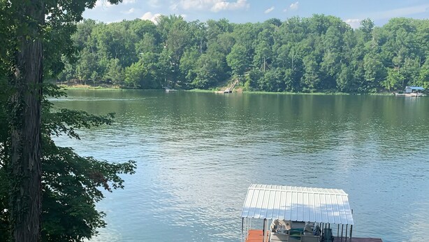 Une jetée en bois mène à une zone abritée où les bateaux peuvent être mis à l’eau, et offre une vue sur un lac et une zone boisée.
