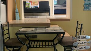 Une cuisine compacte avec une fenêtre donnant sur l’extérieur, une table à manger avec des chaises et un petit îlot central.