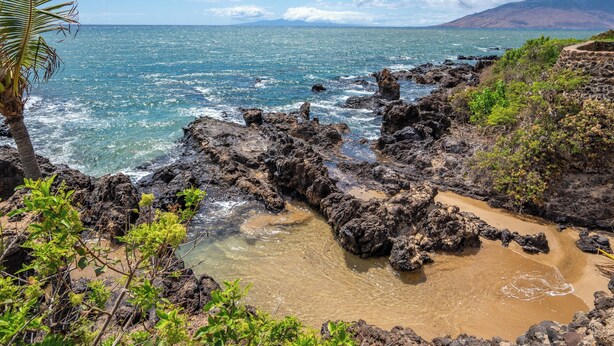 A coastal landscape with rocky terrain, clear blue water, and a distant mountain range. - Top Floor Maui Vista with Ocean View, AC, 5min Walk to Beach (Kihei)