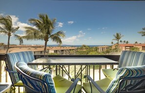 A balcony with striped chairs and a table, overlooking a resort area with palm trees and buildings. - Top Floor Maui Vista with Ocean View, AC, 5min Walk to Beach (Kihei)