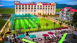 A hotel with a large outdoor tennis court, multiple balconies, and a landscaped garden area. - Mystique Mayong  (Mayang)