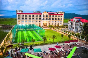 A hotel with a large outdoor tennis court, multiple balconies, and a landscaped garden area.