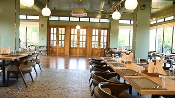 A spacious dining area with high ceilings, large windows, and a mix of wooden and metal furniture.