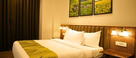 A hotel room with a large bed, two bedside lamps, a headboard with a textured pattern, and three framed paintings on the wall.