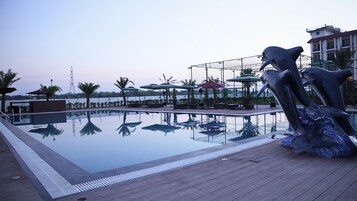 Una piscina con muelle de madera, sillas de descanso, sombrillas y una escultura.