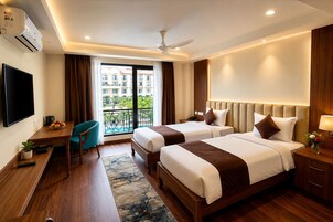 A hotel room with two beds, a desk, a TV, a balcony with a pool view, and an air conditioning unit.