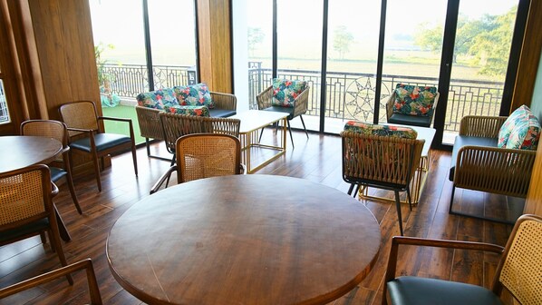 Amplio espacio interior con piso de madera, muebles de mimbre y grandes ventanales con vista a la playa.