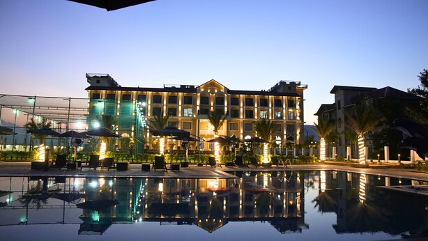A hotel with a large reflective pool, outdoor seating, and a well-lit facade. - Mystique Mayong  (Mayang)