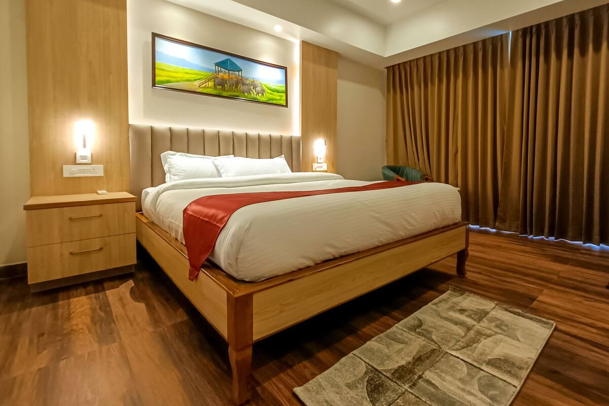 A modern hotel room with a large bed, wooden headboard, and a painting of a farm scene.