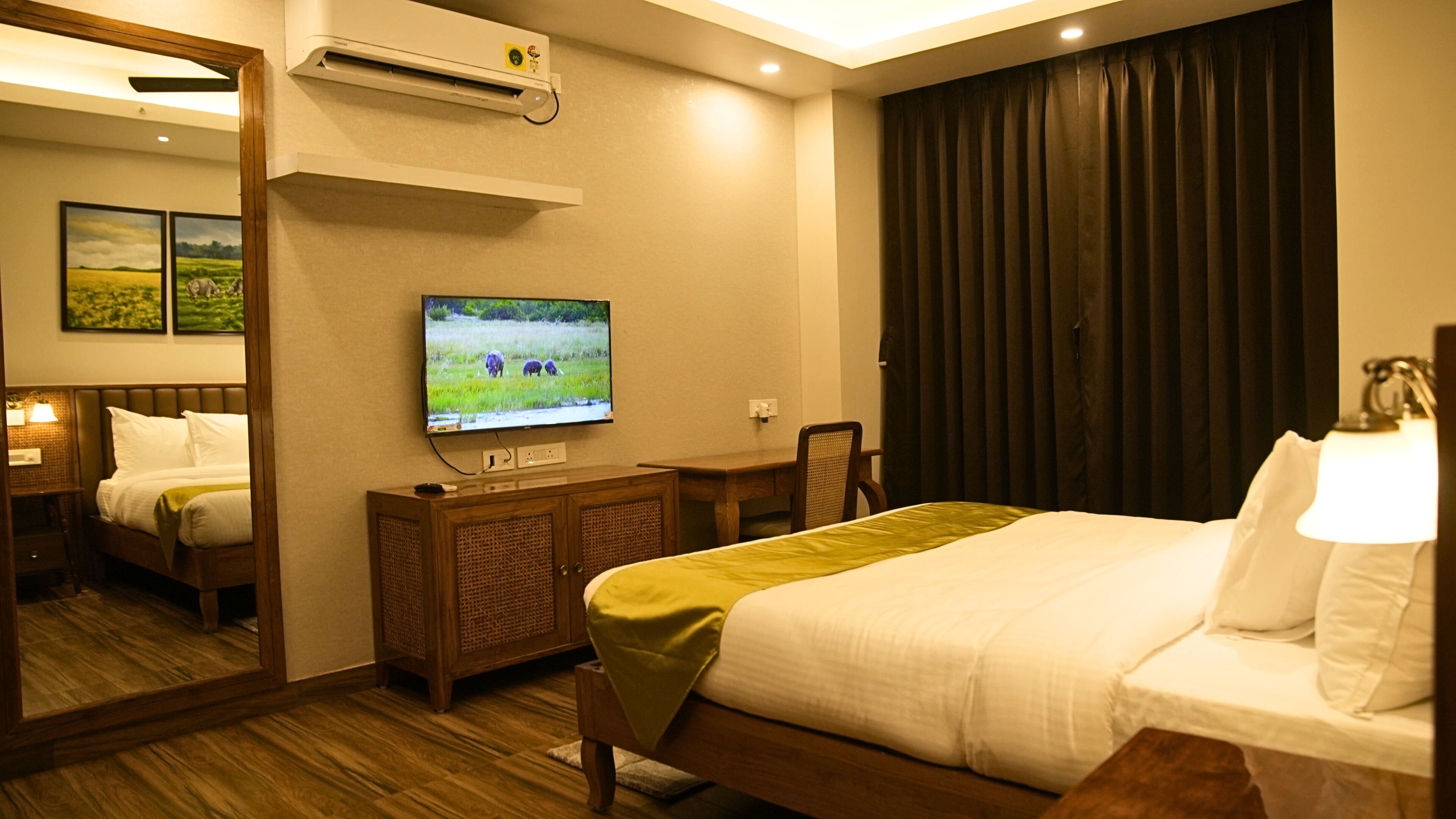 A hotel room with a bed, a desk, a television, a mirror, and a window with curtains.