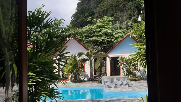 A view of a swimming pool area with two small buildings, surrounded by lush greenery and a mountainous backdrop. - CAT BA PARK HOMESTAY (Hai Phong)