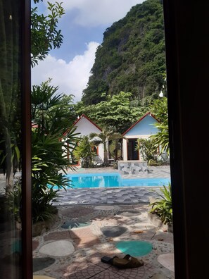 A view of a swimming pool area with two small buildings, surrounded by lush greenery and a mountainous backdrop. - CAT BA PARK HOMESTAY (Hai Phong)