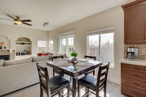 Un salón espacioso con un sofá grande, una mesa de comedor con cuatro sillas y una cocina con armarios de madera y una cafetera.