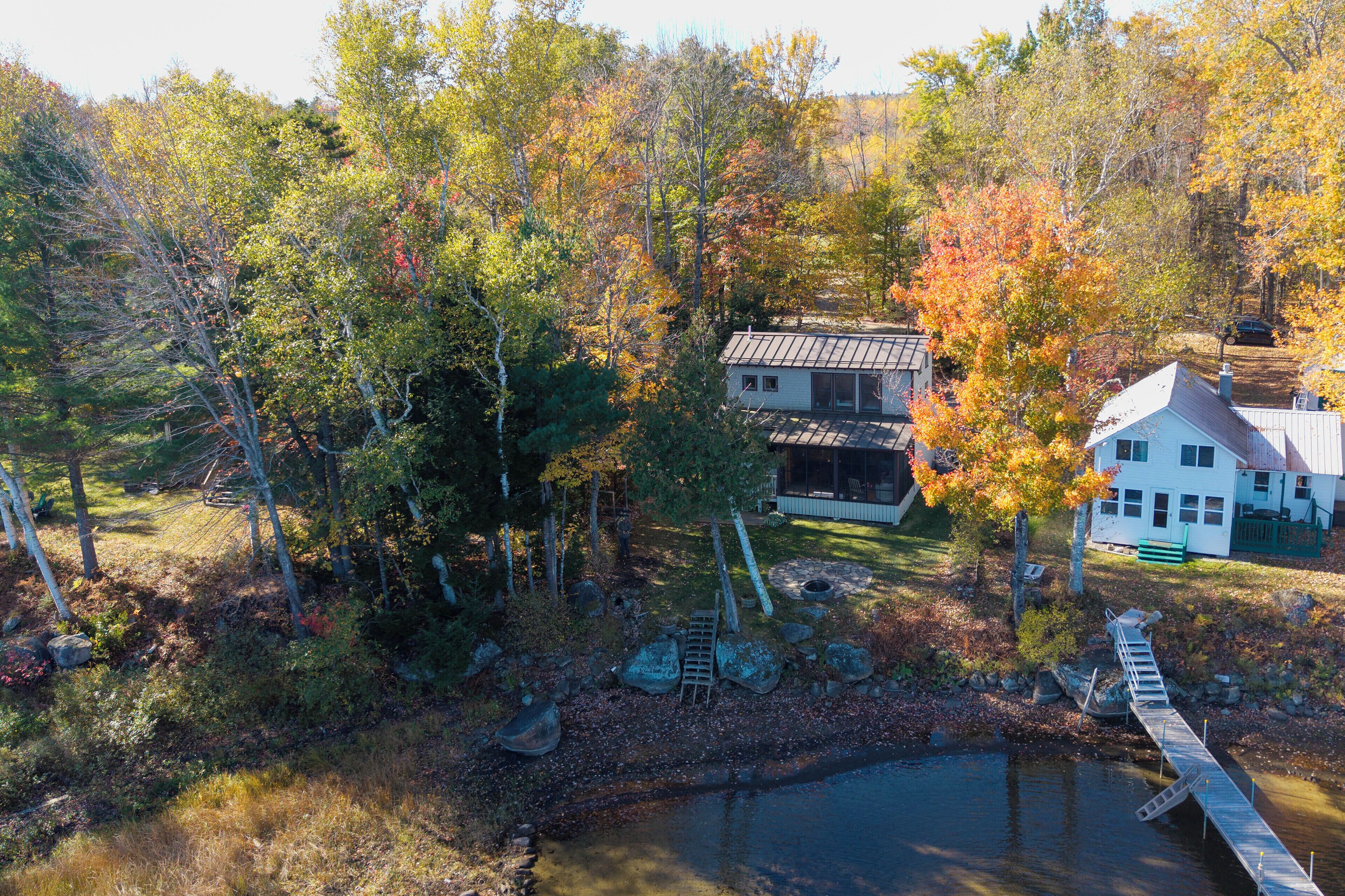A lakeside cabin with a dock, surrounded by autumn foliage.