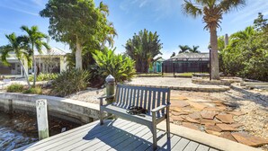 A wooden deck with a bench, palm trees, and a stone pathway. - Port Charlotte Home w/ Private Dock & Pool! (Port Charlotte)
