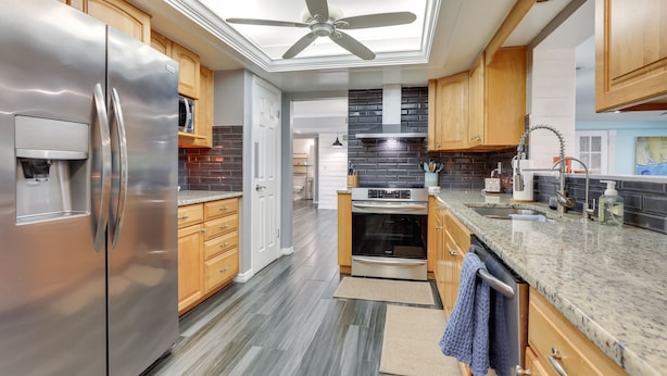 A modern kitchen with stainless steel appliances, wooden cabinets, a skylight, and a granite countertop. - Port Charlotte Home w/ Private Dock & Pool! (Port Charlotte)