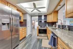 Une cuisine moderne dotée d’appareils électroménagers en acier inoxydable, de meubles en bois, d’un puits de lumière et d’un plan de travail en granit.