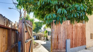Een smalle achtertuin met houten schuttingen, een betonnen pad en een kleine tuin met stoelen en planten.