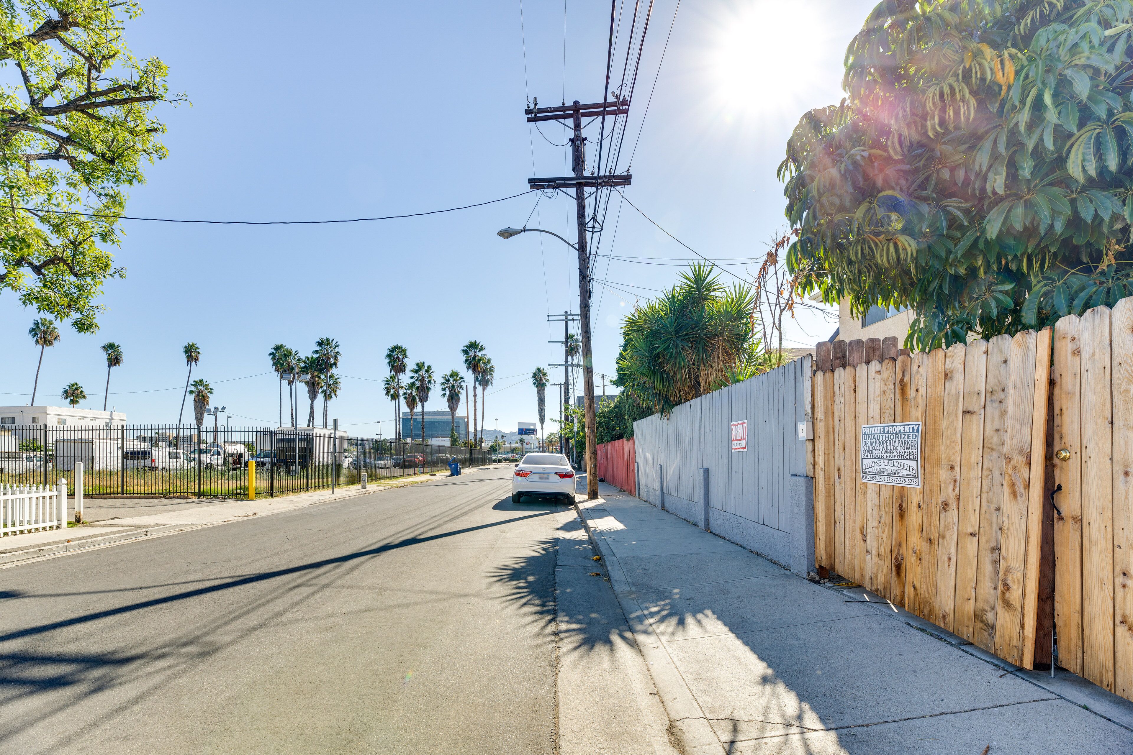 A street with a white car parked on the side, a wooden fence, and a sign indicating private property.