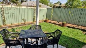 A patio with a table and chairs, surrounded by a green lawn and a wooden deck. - Golden Heritage Accommodation Rutherglen (Rutherglen)