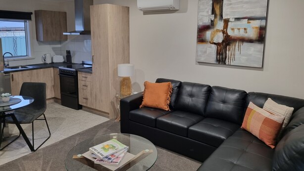 A modern living room with a black leather sofa, a glass coffee table, and a dining area with a black chair. - Golden Heritage Accommodation Rutherglen (Rutherglen)