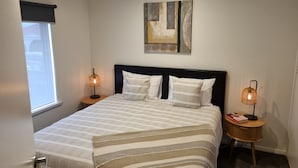 A bedroom with a bed, two bedside tables, a window, and a painting on the wall. - Golden Heritage Accommodation Rutherglen (Rutherglen)