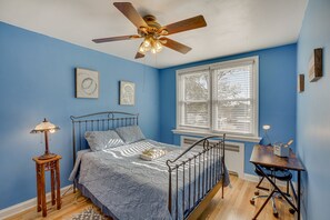 Un dormitorio con cama, escritorio, lámpara de pie y ventilador de techo.