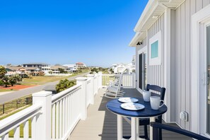 Un balcon avec une table et des chaises, donnant sur une zone côtière avec des maisons et une route.