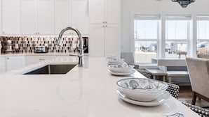 Eine moderne Küche mit weißen Schränken, einer großen Kochinsel mit Spüle und einem Essbereich mit Tisch und Stühlen.