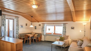 A cozy room with wooden beams, a dining area with a table and chairs, a sofa, and a radiator. - Fewo Nr. 2 Lattenberg für 2-3 Pers., 1 Schlafzimmer, Wohnraum mit Küchenzeile, Balkon (Bischofswiesen)