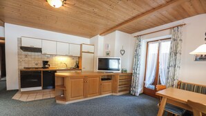 A compact kitchen with wooden cabinets, a built-in oven, and a television. - Fewo Nr. 2 Lattenberg für 2-3 Pers., 1 Schlafzimmer, Wohnraum mit Küchenzeile, Balkon (Bischofswiesen)