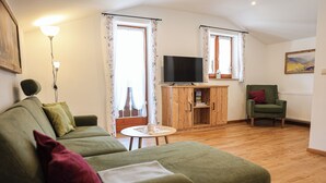 A living room with a green sofa, a green armchair, a wooden cabinet, a television, and a small round table.