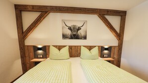Une chambre avec deux lits, une tête de lit en bois, une literie à carreaux et une œuvre d’art sur le thème des taureaux au-dessus des lits.