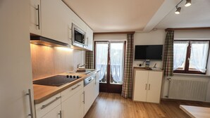 Une cuisine avec des meubles blancs, un four à micro-ondes, une cuisinière et une fenêtre avec des rideaux.