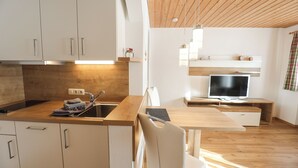 A modern kitchen with white cabinets, a wooden countertop, and a built-in stove. There is a dining area with a wooden table and chairs, and a television on a stand.