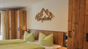 Une chambre avec un lambris en bois, un lit recouvert d’une couette à carreaux verts et un panneau mural décoratif représentant une montagne, sur lequel est inscrit le mot « Berglube ».