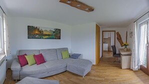 Un salon avec un canapé d’angle gris, un tableau accroché au mur et un plancher en bois.