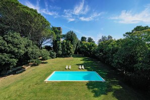 A rectangular swimming pool with two lounge chairs and a grassy lawn, surrounded by dense trees and a clear sky. - Torre delle Cornacchie (Rome)