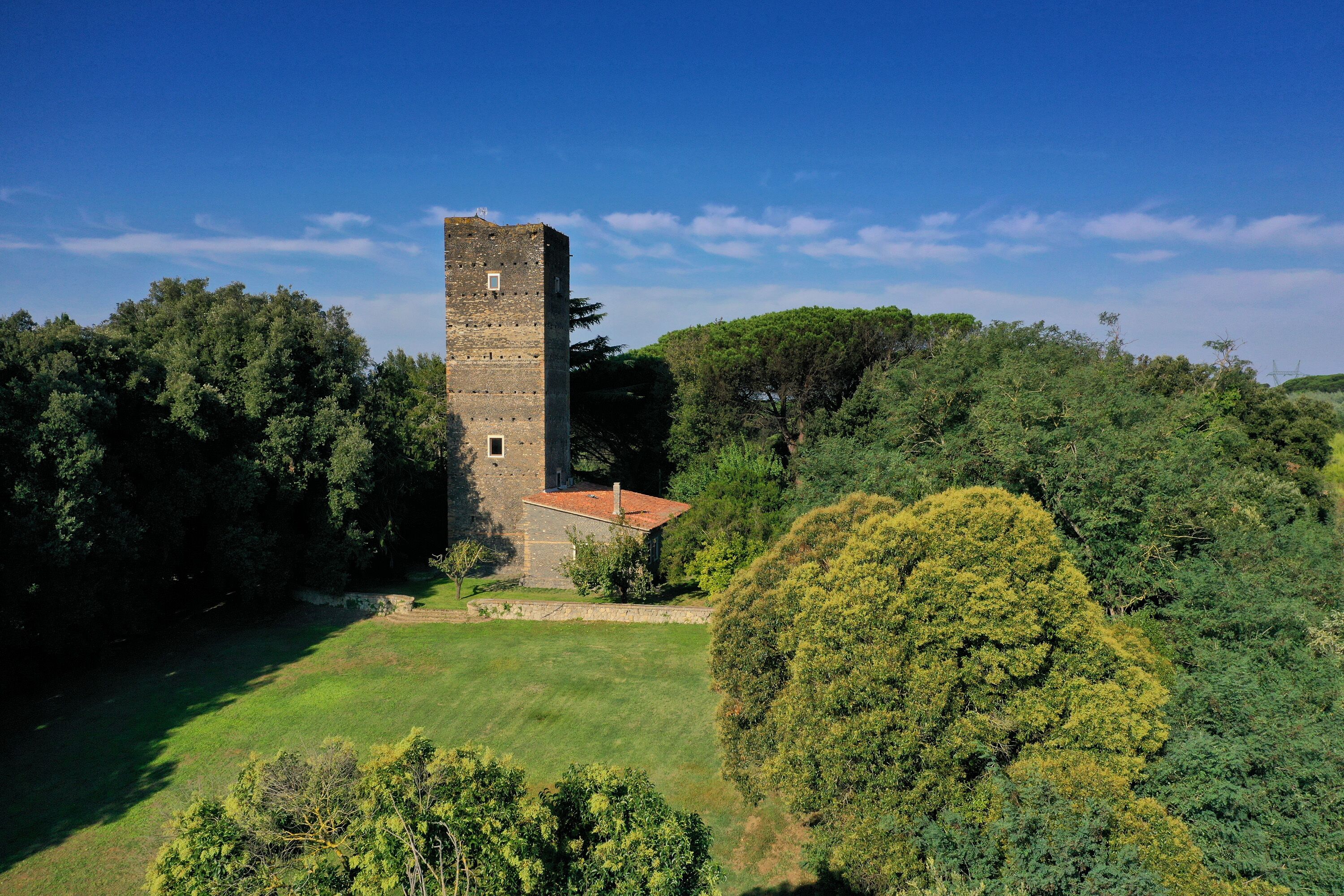 Una torre de piedra histórica con techo rojo, rodeada de abundante vegetación y árboles.