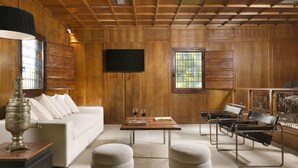 A living room with a wooden ceiling, a flat-screen TV mounted on the wall, a white sofa, a coffee table, and two leather armchairs. - Torre delle Cornacchie (Rome)