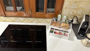 A kitchen with a black induction cooktop, a white countertop, and a wooden cabinet with glass doors. There is a box of bread and a coffee maker on the counter. - 1 Bedroom Apartment in Catania (Catania)