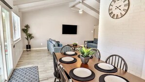 A dining area with a wooden table set for four, a black clock on the wall, and a TV mounted above a sofa. - San Antonio Escape. Close to Lackland, SeaWorld, Fiesta Texas, and Riverwalk (San Antonio)