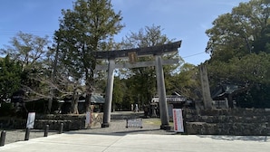 En traditionell japansk torii-port vid ingången till ett tempel, omgiven av stenmurar och träd.