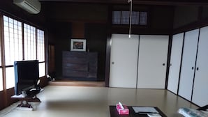 Ett traditionellt japanskt rum med tatamimattor på golvet, ett lågt bord med en ask med näsdukar, en tv och ett skåp med en inramad bild.