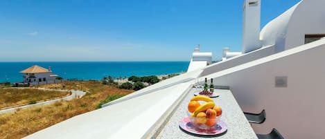 A balcony with a fruit bowl, a bottle of wine, and a view of the sea.